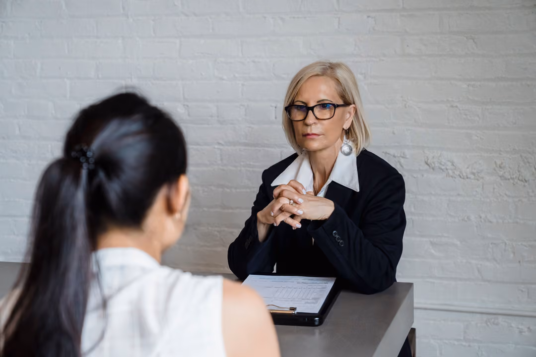 A senior leader listens closely across a desk during a candid one-on-one assessment conversation.