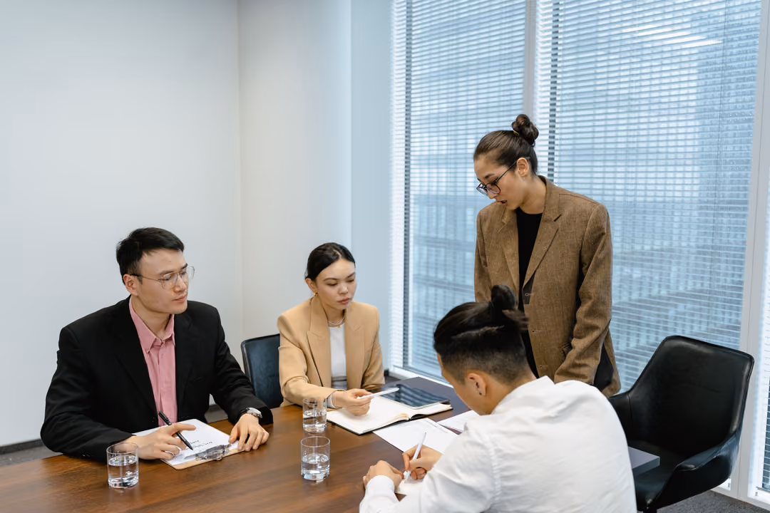A small management team meets around a table in a glass-walled office, reviewing a decision together.